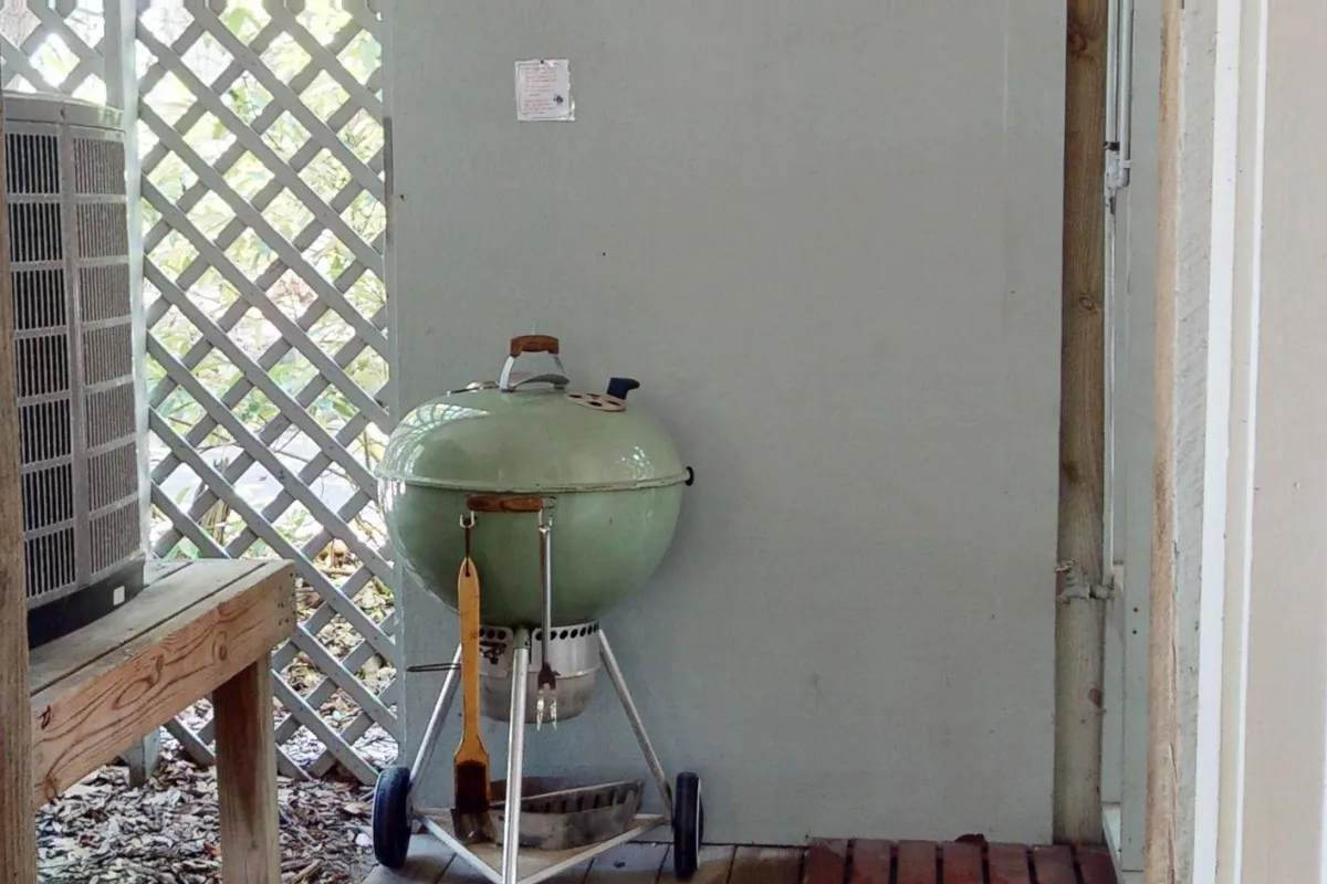 An interior/outdoor space with a green charcoal grill set on a wooden table against a lattice wall, creating a cozy area for barbecuing and dining. The setup is inviting and tailored for group gatherings or family cookouts.