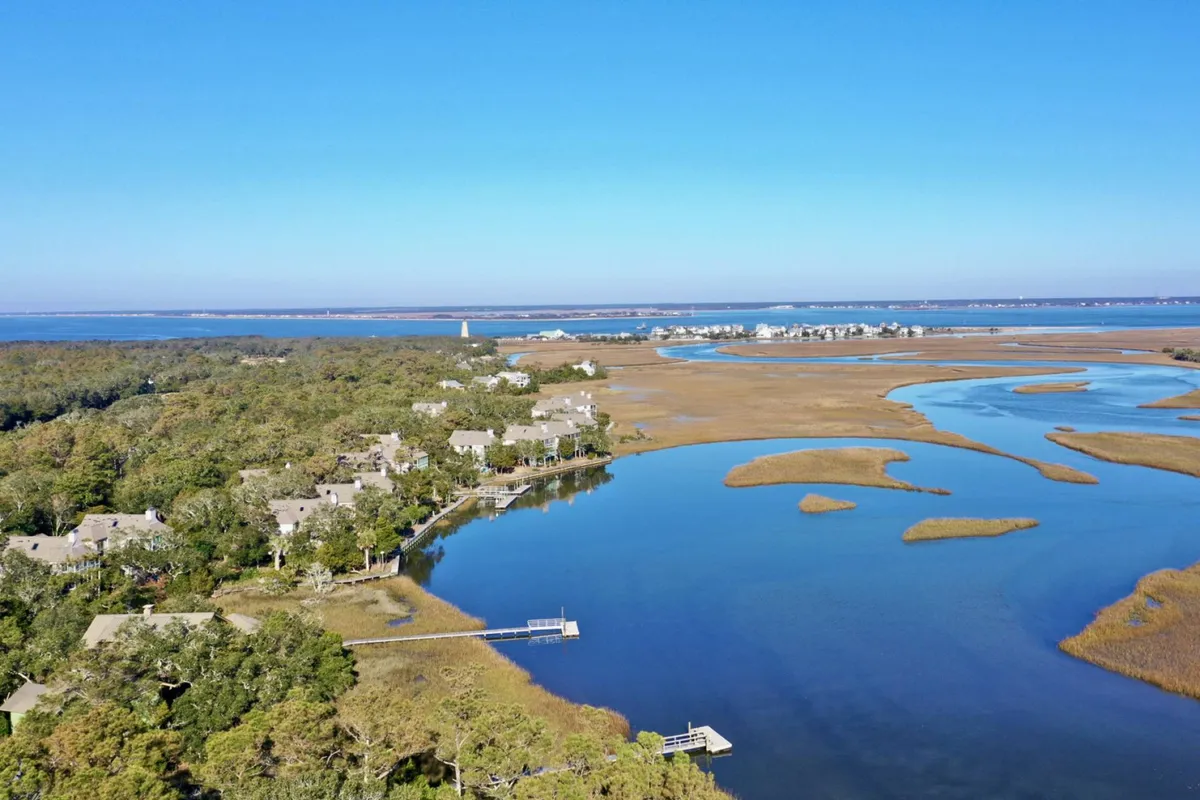 This view captures calm waters, expansive marshland, a distant lighthouse, and homes along the shoreline. The wide vista offers a sense of the surrounding area and highlights the abundance of wildlife and natural beauty waiting just beyond the porch.