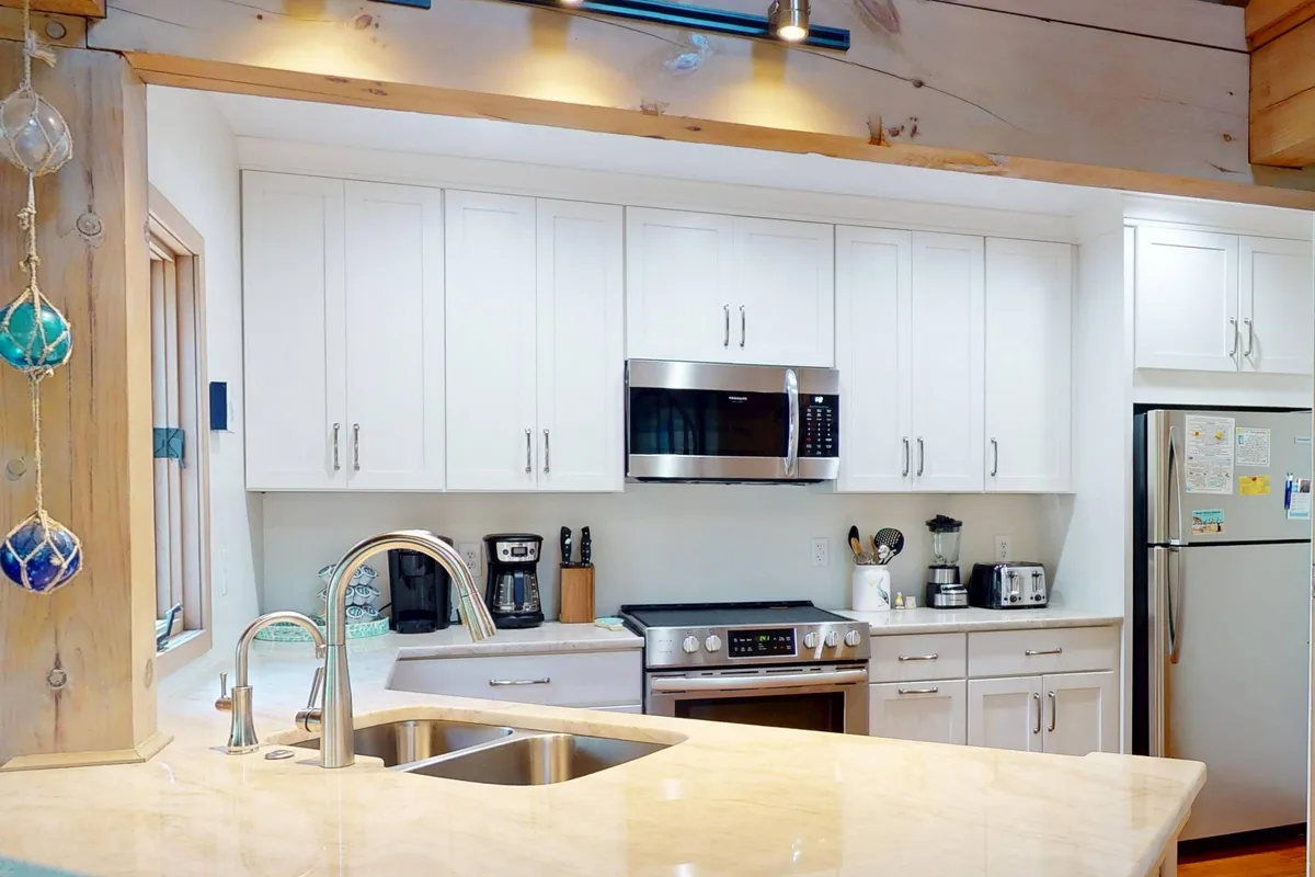 A modern kitchen featuring a large island, white cabinetry, stainless steel appliances, and a sink with a modern faucet. The kitchen is airy and functional, seamlessly connecting to the living and dining spaces for effortless entertaining and meal preparation.