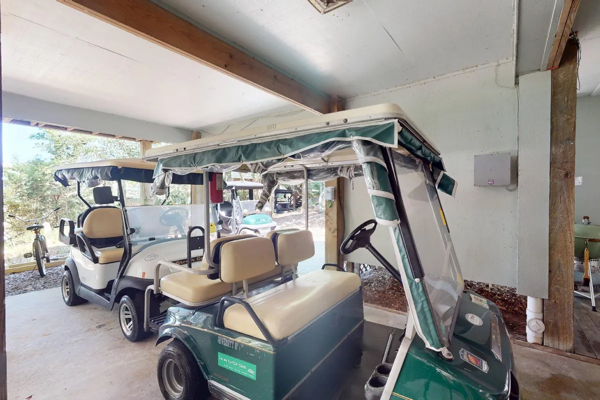 This interior image prominently displays two golf carts parked inside a spacious garage area, with a bicycle visible in the background. The setting is practical and tidy, emphasizing ease of access to transportation and the car-free island lifestyle.