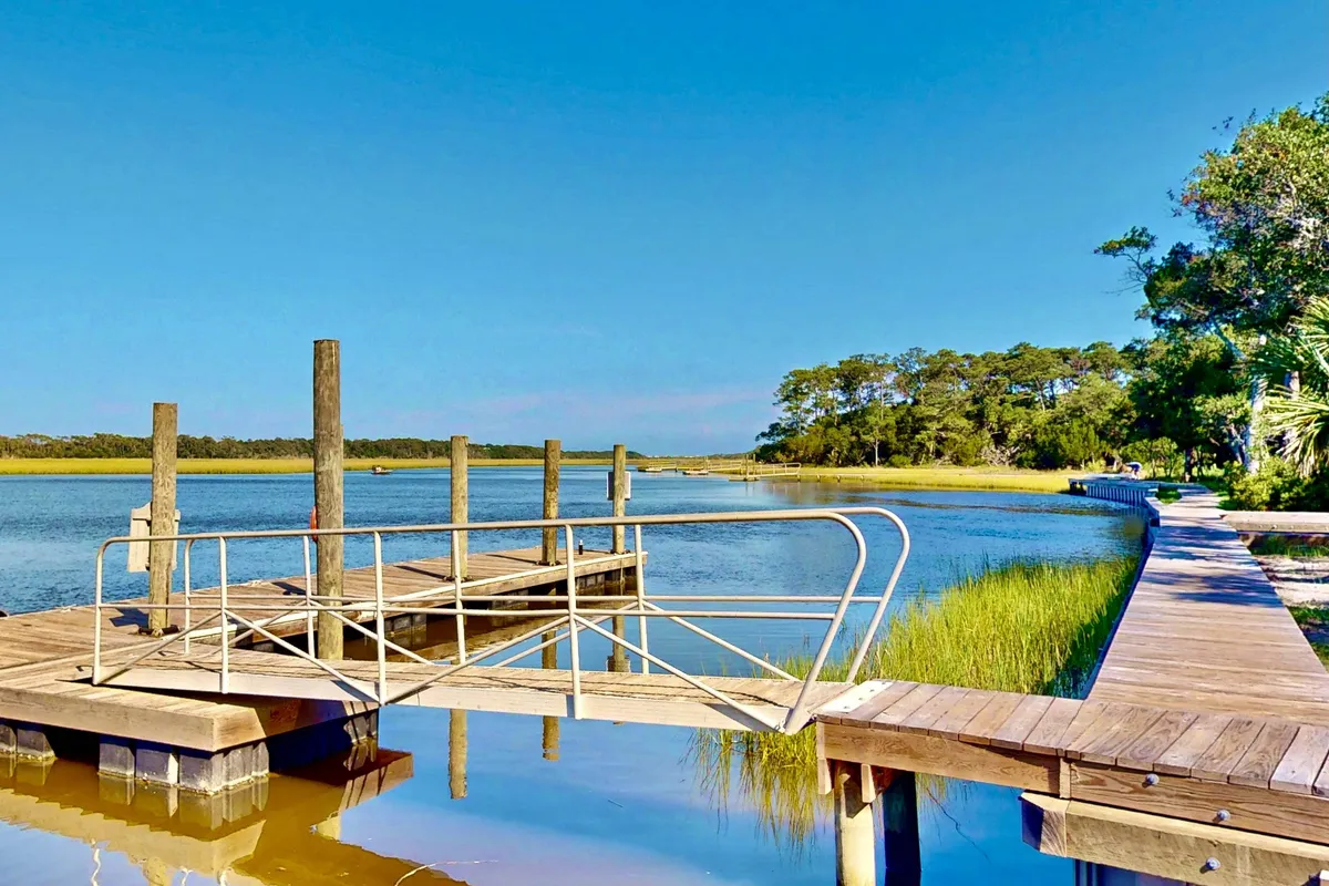 An exterior view of a dock stretching out over calm water, bordered by natural vegetation and open sky. The peaceful scene invites activities like fishing, boating, or simply relaxing by the shore.