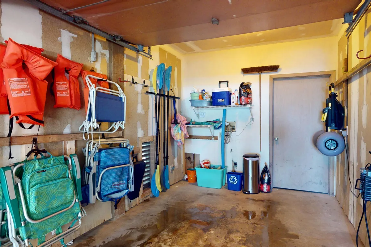 A functional interior storage space featuring life jackets, kayak paddles, beach chairs, and organized shelving. The area is clearly set up for storing and preparing beach and outdoor adventure gear.
