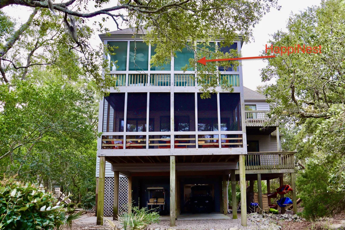 This exterior shot features a spacious balcony supported by structural pillars, surrounded by lush greenery. The setting is casual and inviting, with plenty of space for relaxing, entertaining guests, or simply enjoying the outdoors.