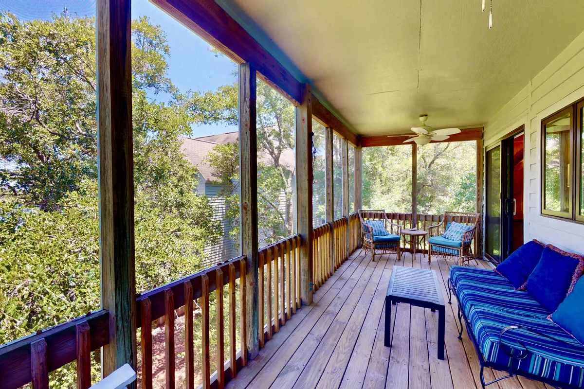 A tranquil screened porch with comfortable seating, wooden flooring, and clear views through screened panels to the marsh beyond. The porch is bathed in natural light, inviting guests to relax, read, or enjoy birdwatching without worrying about bugs.