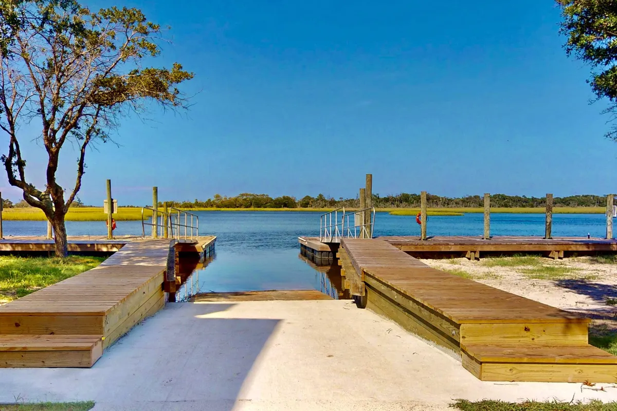 A tranquil wooden dock stretches out over calm water, framed by surrounding trees. The setting is ideal for nature walks, boating, or simply taking in the peaceful scenery and watching for wildlife.