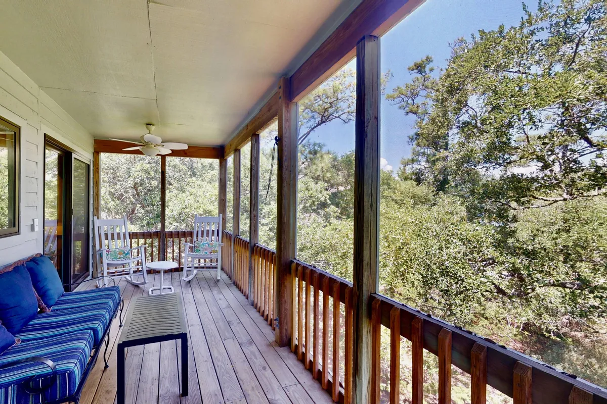 This image features a classic screened porch with inviting rocking chairs, a striped couch, and a wooden railing overlooking lush greenery. The porch exudes tranquility, providing a welcoming space to relax, read, converse, or simply soak in the sounds of nature.